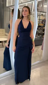 Vestido largo azul marino con acabado brillante, escote halter pronunciado y aberturas laterales en la cintura con detalle de nudo drapeado en la falda.