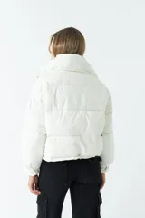 Campera puffer cropped color blanco, de corte a la cintura, con cuello alto, cierre metálico frontal con botones a presión y bolsillos laterales con cierre invisible.