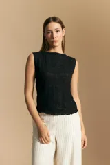 Top sin mangas de jacquard color negro, con cuello cerrado y silueta recta. Presenta una textura trabajada con relieve y una terminación suavemente ondulada en el ruedo.