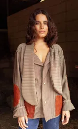 Blazer de corte oversize confeccionado en tela casimir a rayas, con cuello tipo lazo y parches de cuero en los codos y bolsillos frontales.