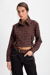 Camisa corta estilo corset de color blanco, con cuello clásico, cierre frontal de botones y detalles de cordones laterales ajustables. Presenta pinzas frontales y traseras para un ajuste entallado.