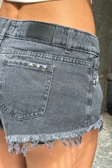 Short de jean tiro bajo, color negro lavado, con roturas y terminación deshilachada en el ruedo. Presenta detalles de apliques metálicos en forma de estrella en los bolsillos delanteros.