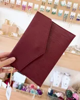 Sobre de fiesta color bordó con textura acanalada y solapa triangular. Incluye una correa de mano corta.