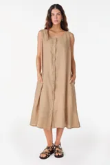 Vestido midi de lino color beige, sin mangas, con escote redondo, abotonamiento frontal completo, bolsillos laterales y corte holgado.