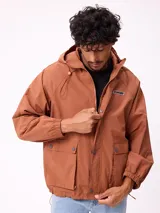 Campera impermeable Rusty de nylon con capucha, cierre frontal y botones a presión. Presenta bolsillos frontales con solapa, puños elásticos y logo de la marca en el pecho.