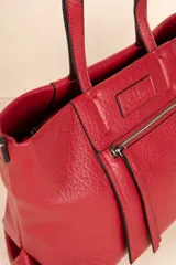 Cartera tipo tote bag de símil cuero texturizado color rojo, con asas fijas y correa larga desmontable y regulable. Posee un bolsillo exterior con cierre metálico y tres compartimientos internos.