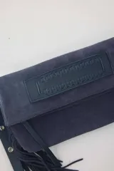 Cartera bandolera de gamuza azul marino con flecos en los laterales y solapa frontal decorada con detalle de cuero liso. Cuenta con asa ajustable y herrajes metálicos plateados.