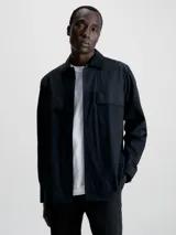 Camisa negra de popelina con corte relaxed, cierre frontal con botones, mangas largas y dos bolsillos con solapa en el pecho.