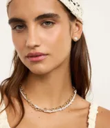 Conjunto de accesorios que incluye un collar doble compuesto por una cadena de eslabones dorados y un collar de perlas, acompañado de un par de aros con diseño de concha marina en tono dorado.