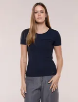Remera básica de modal elastizado color blanco, con textura acanalada fina, escote redondo y mangas cortas. Presenta un pequeño logo metálico aplicado cerca del ruedo frontal.