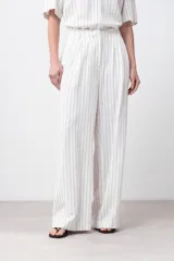 Pantalón de lino color blanco con finas rayas verticales negras, corte palazzo, cintura alta con pinzas y cinturón marrón.