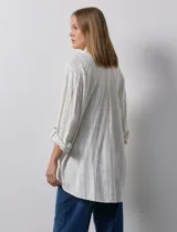 Camisa de lino a rayas verticales color crema, con cuello con solapa, abertura central con botones, bolsillos delanteros y mangas 3/4 regulables con presilla y botón.