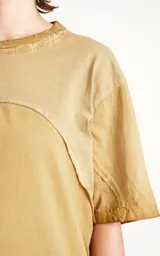 Remera oversize de algodón, color mostaza con efecto batik artesanal. Presenta costuras decorativas arqueadas que unen el cuello con los hombros y el torso.