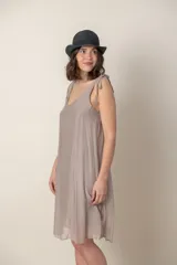 Vestido corto de seda color gris oscuro, con escote redondo y tirantes anudados en los hombros. El calce es suelto y la tela es ligeramente transparente.