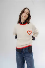 Buzo de punto color crema con detalles en rojo en el cuello, puños y ruedo. Presenta un bolsillo frontal en el pecho con un corazón bordado en relieve.