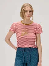 Remera baby tee de algodón con diseño a rayas horizontales en rojo y blanco, cuello redondo en tono tostado y gráfico impreso en el pecho. Cuenta con mangas cortas y terminaciones con volados sutiles en mangas y ruedo.