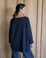Remerón de corte oversize color beige, con cuello redondo, mangas largas y diseño asimétrico con la parte trasera más larga que la delantera y aberturas laterales en el ruedo.