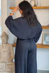 Conjunto de camisa y pantalón de viscosa negro con finas líneas metalizadas doradas. La camisa es de manga larga con escote en V y botones frontales, mientras que el pantalón es de corte ancho y tiro alto con cintura elástica fruncida.