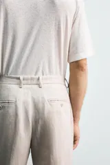 Pantalón de traje regular fit confeccionado en tejido de lino, con bolsillos laterales y bolsillos traseros de vivo con botón. Presenta cierre frontal con cremallera y botón.
