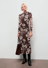 Vestido midi de corte entallado con cuello asimétrico y manga larga. Presenta un diseño drapeado en la cintura y un estampado floral sobre fondo oscuro.