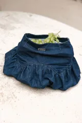 Pollera corta de jean oscuro, estilo 'balloon' o globo, con fruncido amplio en la parte inferior y pretina ancha con etiqueta de marca.