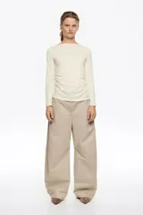 Pantalón de algodón color beige, de corte barrel ancho con tiro bajo. Presenta bolsillos en costuras delanteros y con vivo en la parte trasera. El bajo de la pierna tiene trabillas para ajustar el volumen.