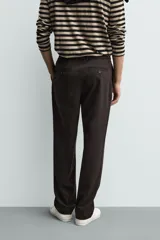 Pantalón de corte recto confeccionado en tejido elástico, con cintura elástica, pliegues frontales, bolsillos laterales y bolsillos traseros de vivo con botón.