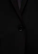 Blazer negro de corte recto y estilo sastre, con cuello de solapa con muesca, cierre frontal de un botón, mangas largas con puños abotonados y dos bolsillos delanteros con solapa.