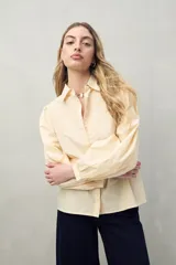 Camisa color crema con bordado floral en el frente, cuello clásico, mangas largas abullonadas con puños abotonados y cierre frontal con botones.