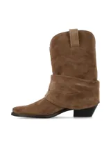 Bota de caña media confeccionada en gamuza color marrón, con diseño de pliegues naturales y caída suave. Presenta punta afinada y taco acuñado, con un estilo inspirado en la estética western.