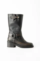 Bota de caña media confeccionada en cuero con efecto gastado manual. Presenta punta cuadrada, taco bloque y detalle de tira con hebilla en la parte superior de la caña, además de una tira decorativa con argolla metálica y remaches en la zona del tobillo.