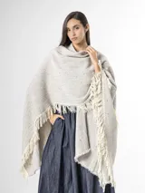 Ruana de punto color beige con sutiles motas multicolores, con bordes terminados en flecos largos.