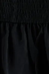 Vestido corto negro en tejido fruncido, de ajuste entallado con hombros descubiertos, escote cuadrado elástico y volado ancho con volumen en escote y bajo.