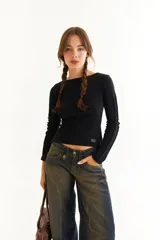 Top de manga larga color marrón, confeccionado en tejido acanalado con cuello bote. Presenta costuras decorativas expuestas a lo largo de las mangas, creando un efecto de relieve.