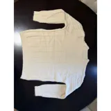 Sweater de punto color crema con diseño de trenzas y rombos, cuello redondo y mangas largas. Presenta un pequeño aplique decorativo en el pecho.