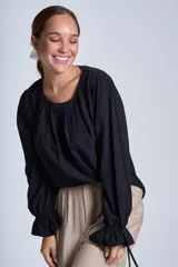 Blusa de manga larga color rosado, con cuello redondo y puños elásticos con volados y lazos decorativos. Presenta un diseño holgado con frunces en el escote.