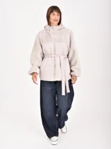 Campera gris claro con capucha, mangas y parte superior de tejido tipo borrego, y parte inferior acolchada con cinturón para ajustar en la cintura. Cierre frontal con cremallera.