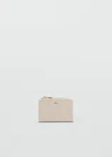 Billetera compacta de poliuretano en color beige, con diseño trenzado y cierre de cremallera superior. Cuenta con detalles metálicos dorados y el logo de la marca grabado en el frente.