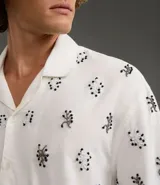 Camisa de manga corta para hombre, corte boxy, color blanco con cuello bowling y un estampado repetitivo de figuras geométricas negras.