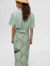 Pareo largo de viscosa en color verde menta, con diseño estampado que presenta gráficos abstractos y una figura central destacada en negro. Es una prenda liviana y fresca, ideal para usar sobre el traje de baño o como falda envolvente.