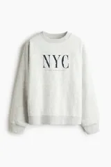 Buzo de cuello redondo con diseño estampado frontal con texto NYC y Lower Manhattan. Presenta hombros caídos, mangas largas y terminaciones acanaladas en puños y ruedo.