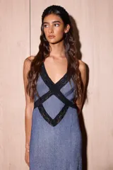 Vestido largo de silueta fluida, entallado en el torso, con escote profundo en V y espalda descubierta con tiras cruzadas. El cuerpo del vestido es de tejido jersey con lurex azul, y la falda presenta paneles triangulares de encaje negro con diseño de lunares.