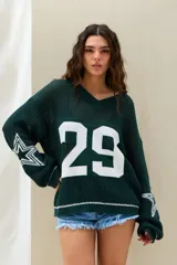 Sweater de punto color verde oscuro, con diseño oversize, mangas largas con estrellas blancas estampadas y la inscripción "BOSTON 29" en la espalda.