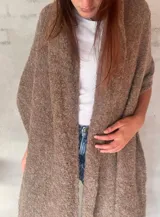 Chal de punto bouclé color marrón claro, hecho de 100% baby alpaca. Tejido suave, esponjoso y cálido, ofrece una textura envolvente y lujosa.