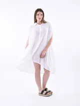 Vestido camisero de corte oversize y silueta asimétrica, confeccionado en tela texturizada color blanco. Presenta cuello clásico, cierre frontal con botones y mangas cortas integradas.