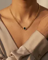 Collar de cadena tipo eslabones gruesos con baño de oro, que presenta un dije central circular con incrustación de piedra ónix negra.