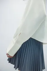 Camisa de manga larga con cuello clásico y botonadura frontal. Presenta una corbata extraíble a juego, puños con cierre de botón y un sutil detalle bordado en el pecho. El diseño incluye un canesú con pliegue en la espalda y un bajo redondeado con aberturas laterales.