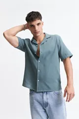 Camisa de manga corta con cuello cubano, confeccionada en tejido con textura. Presenta un corte regular y cierre frontal con botones.