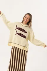 Sweater color manteca de tejido de punto con cuello redondo y ribete marrón. Presenta dos peces marrones tejidos en el frente con detalles bordados a mano.