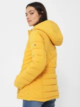 Campera amarilla acolchada con capucha, cierre frontal con cremallera, bolsillos laterales y logo de Tommy Hilfiger en el pecho.
